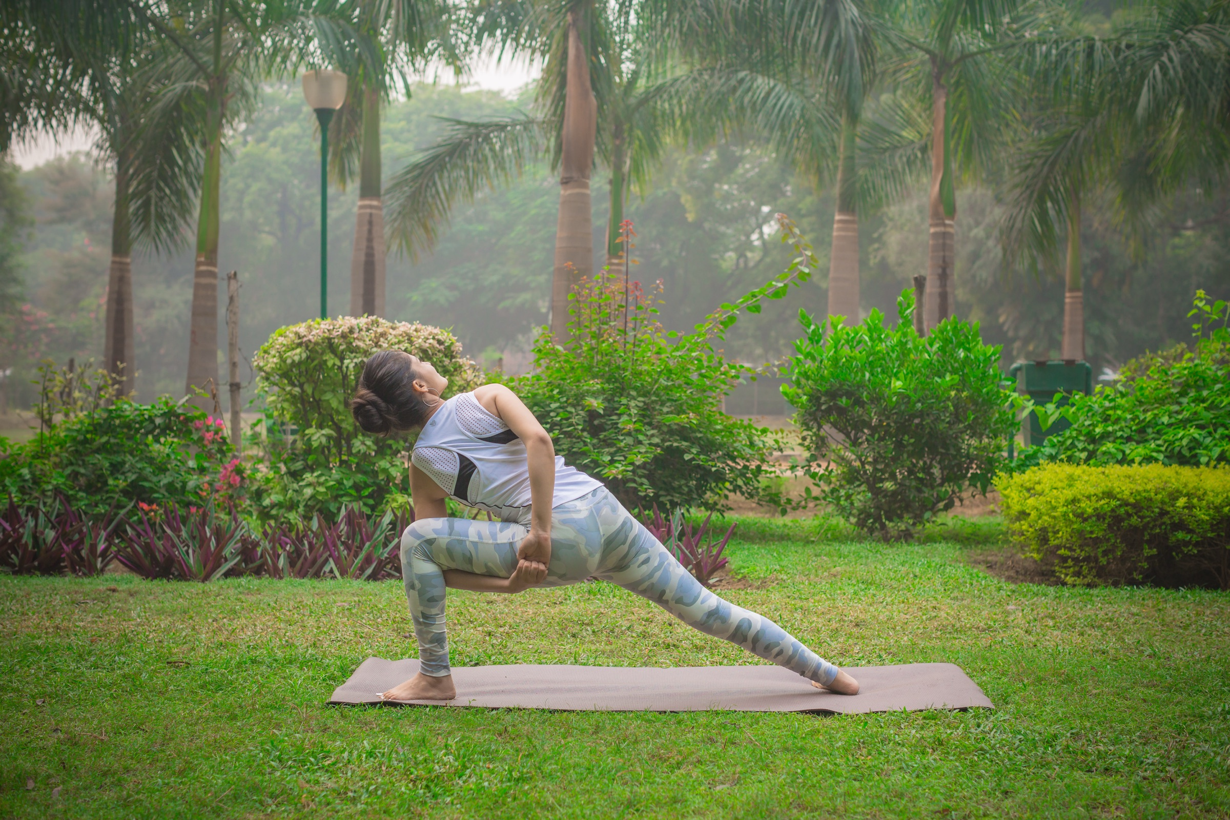 Surgeet in a twisted side-angle lunge on the grass beneath palm trees